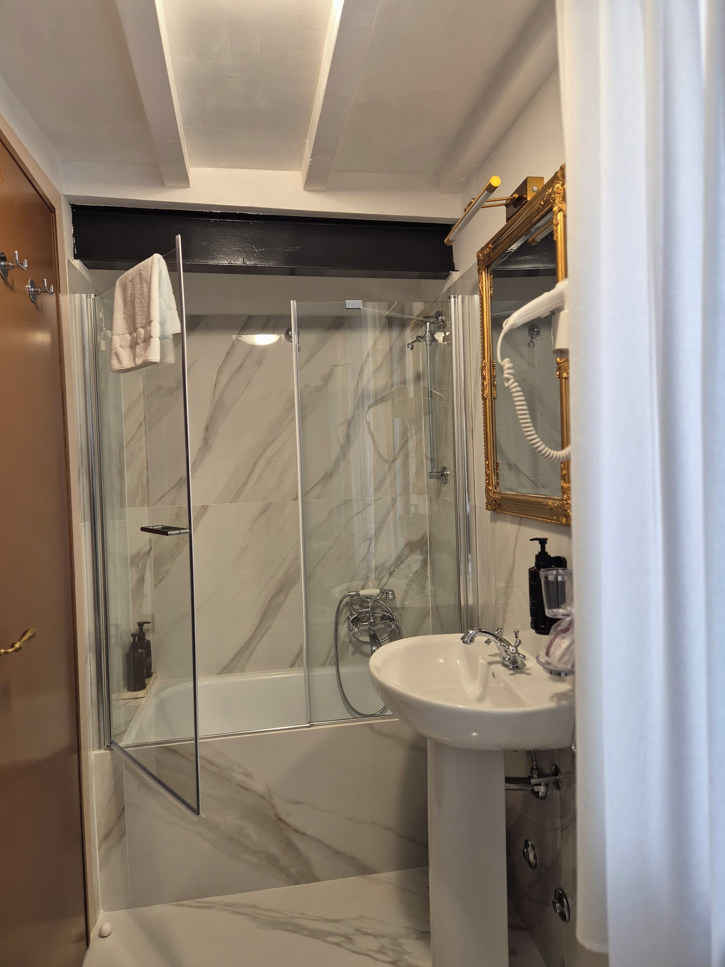 A bathroom with a glass-enclosed shower, a white sink, and a gold-framed mirror.