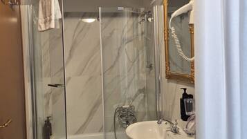 A bathroom with a glass-enclosed shower, a white sink, and a gold-framed mirror.