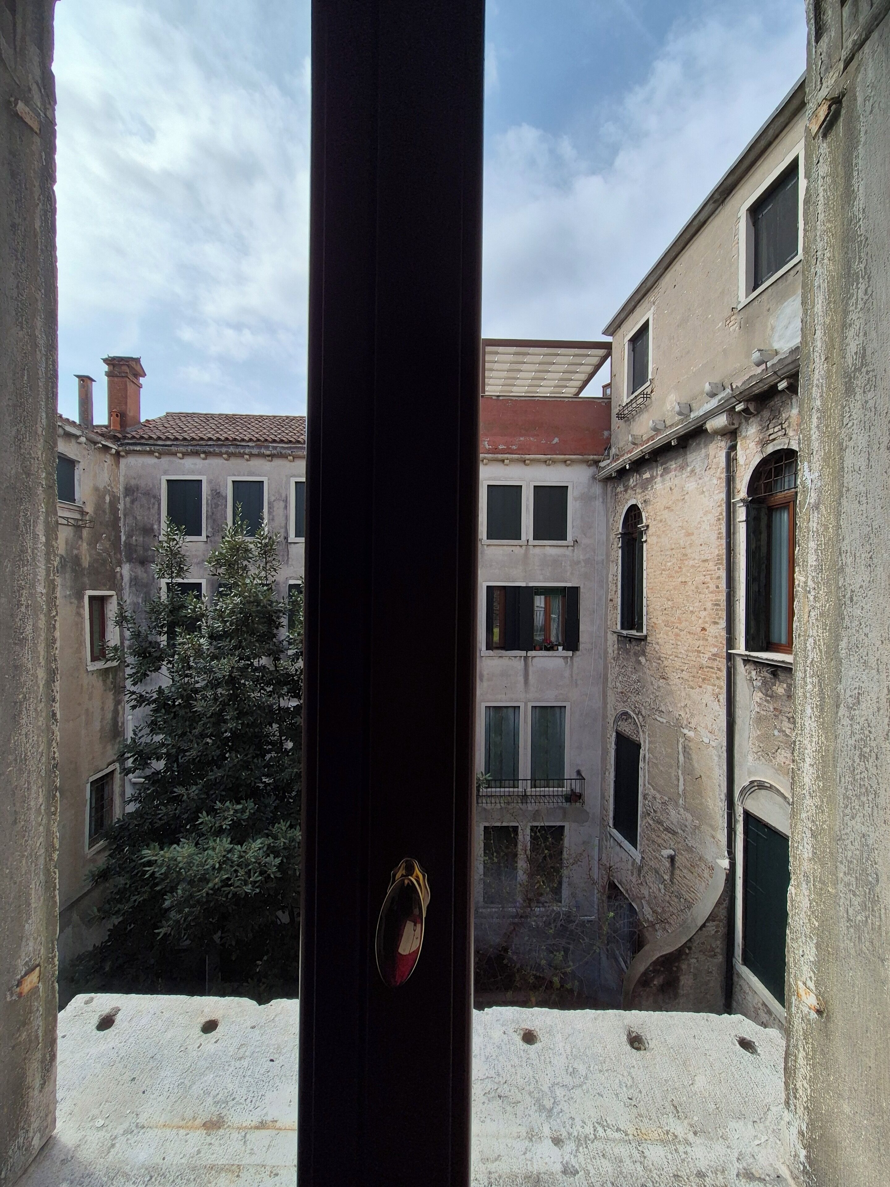 A narrow alleyway with buildings on either side, a tree in the center, and a door with a keyhole in the foreground.