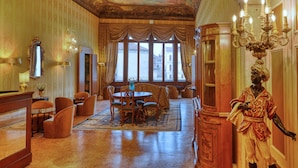 A grand room with a large chandelier, ornate ceiling, and a statue. There is a table with chairs and a window with curtains. - PALAZZO MALIPIERO TREVISAN - LE TRE DIMORE D'EPOCA (Venice)