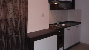 A small kitchen with white cabinets, a black countertop, and a stainless steel sink. - Apartments Snježana (Sali)