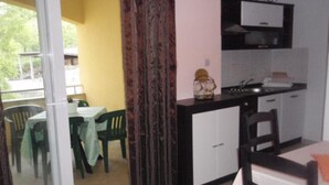 A compact kitchen with a dining area, a sliding glass door leading to an outdoor space, and a small table with chairs. - Apartments Snježana (Sali)