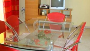 A modern living room with a glass-top coffee table, red chairs, a flat-screen TV, and a wooden cabinet. - Apartments Snježana (Sali)