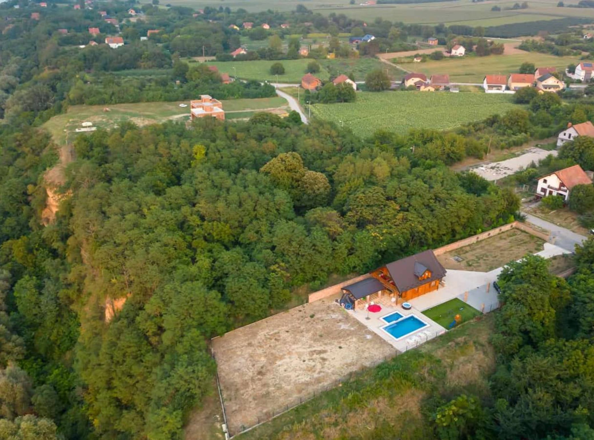 Vista aérea de una zona rural con casas dispersas, un extenso campo abierto y un edificio con piscina y zona de estar al aire libre.