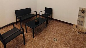 Una habitación con suelo de baldosas, un sofá negro, una pequeña mesa y luces colgantes.