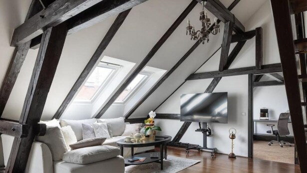 A loft-style room with exposed wooden beams, a modern sofa, a round coffee table, and a flat-screen TV. - Zagreb Downtown Luxury Stay – 5th Element (Zagreb)
