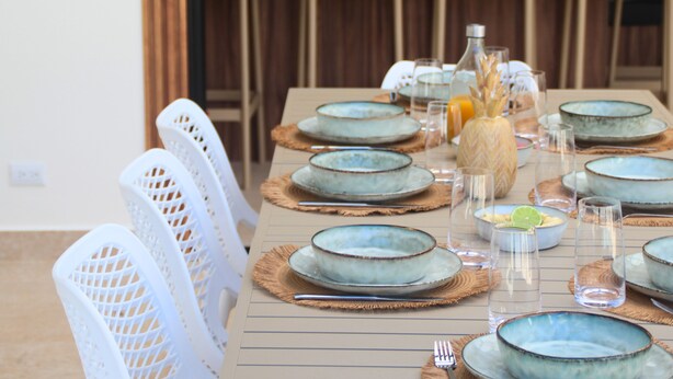 A dining table set with blue plates, white chairs, and a centerpiece with a vase and fruit. - Villa 3 suites, private pools, comfort & relaxation (Provincia de guanacaste)