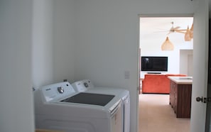 Ein Waschraum mit zwei weißen Waschmaschinen, eine Küche mit einem roten Sofa und einem an der Wand befestigten Fernseher.