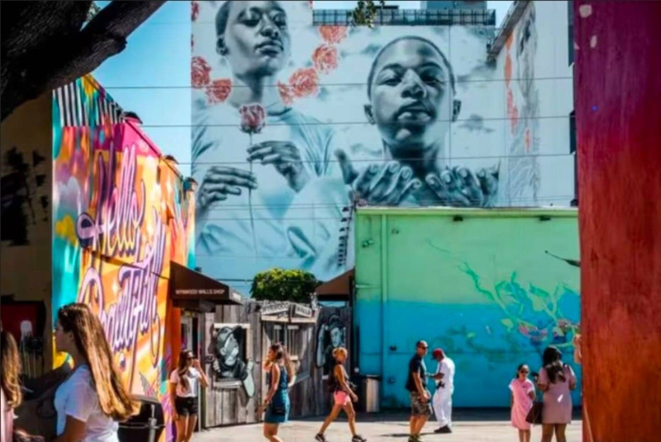 A street with a large mural, shops, and people walking.