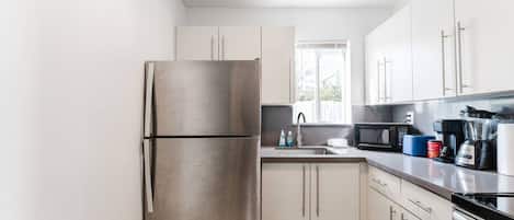 Une cuisine moderne dotée d’appareils électroménagers en acier inoxydable, de meubles blancs et d’une fenêtre laissant entrer la lumière naturelle.