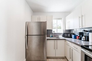 A modern kitchen with stainless steel appliances, white cabinetry, and a window providing natural light. - Wynwood Escape|2BR+Free Parking & Miami Vibes! (Miami)