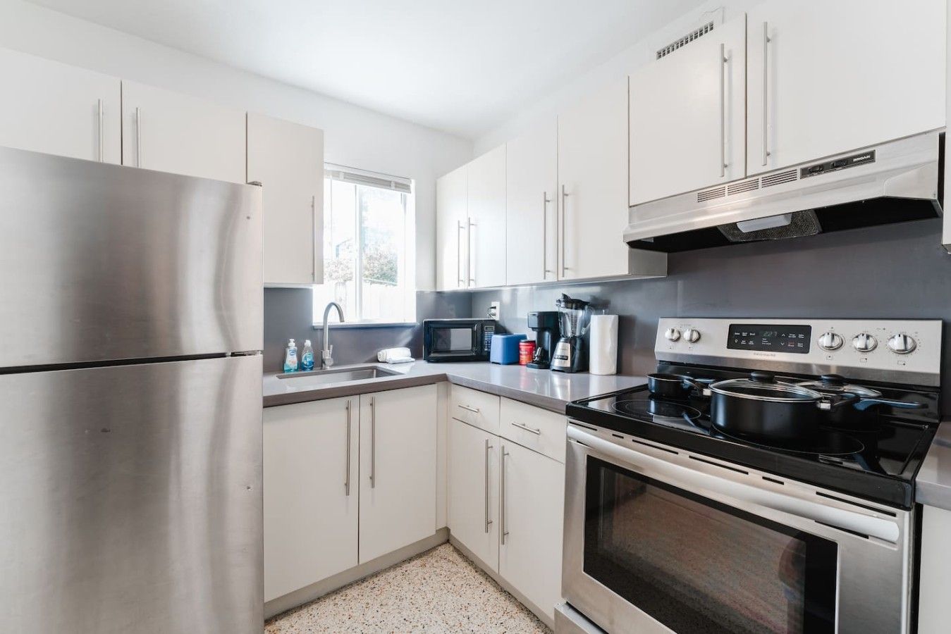 A modern kitchen with stainless steel appliances, white cabinetry, and a window providing natural light.