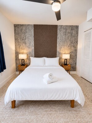 A hotel room with a large bed, two bedside lamps, a ceiling fan, and a textured wall. - Wynwood Escape|2BR+Free Parking & Miami Vibes! (Miami)