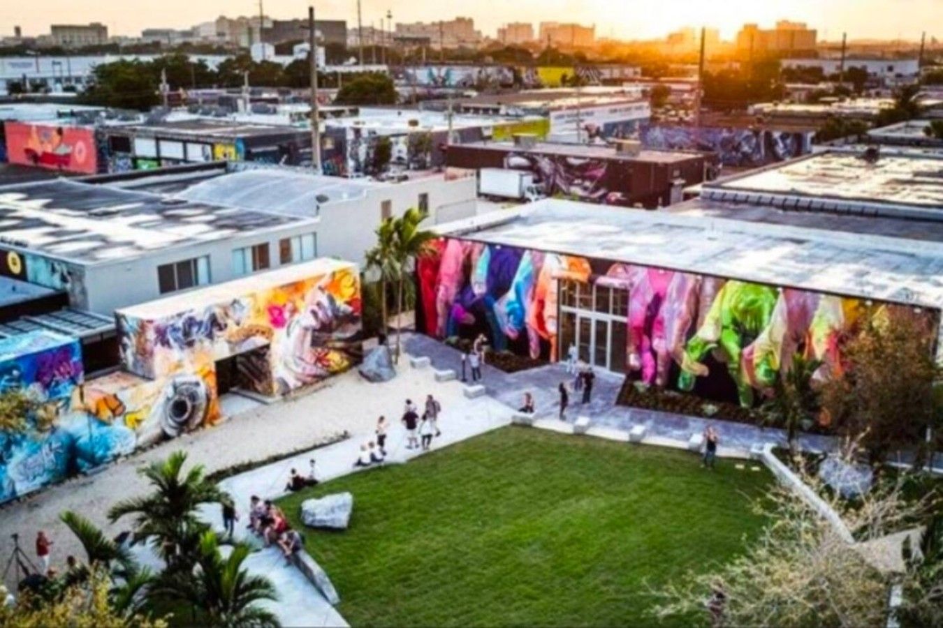 A building with a colorful mural on the exterior wall, a grassy courtyard, and a parking area.