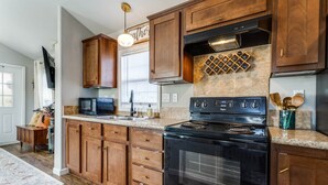 A kitchen with wooden cabinets, a black stove, a microwave, and a wine rack. - Luxury Amenity-loaded Tiny Home w/ Pet Yard +EVCharg (Collin County)