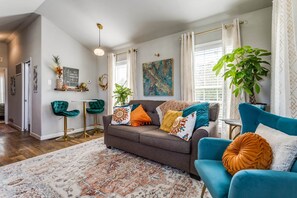 Een woonkamer met een bruine bank, een blauwgroene fauteuil, een vloerkleed met dessin en decoratieve kussens.