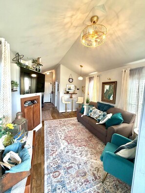 A spacious living area with a large sofa, a television, and a patterned rug. - Luxury Micro Retreat| Spa Amenities|Fire Pit|Pet Yard (Collin County)