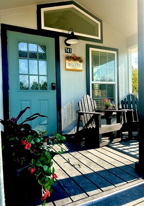A porch with a blue door, two Adirondack chairs, and a small table with a potted plant.