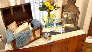 A wooden cabinet with a lace tablecloth, a vintage lantern, a framed picture, and a vase with yellow flowers. - Luxury Amenity-loaded Tiny Home w/ Pet Yard +EVCharg (Collin County)