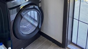 A laundry area with two stacked washers and dryers, a fire extinguisher mounted on the wall, and a sliding glass door leading outside. - Secluded Contemporary 2BR 2BA Suite (Dundas Town)