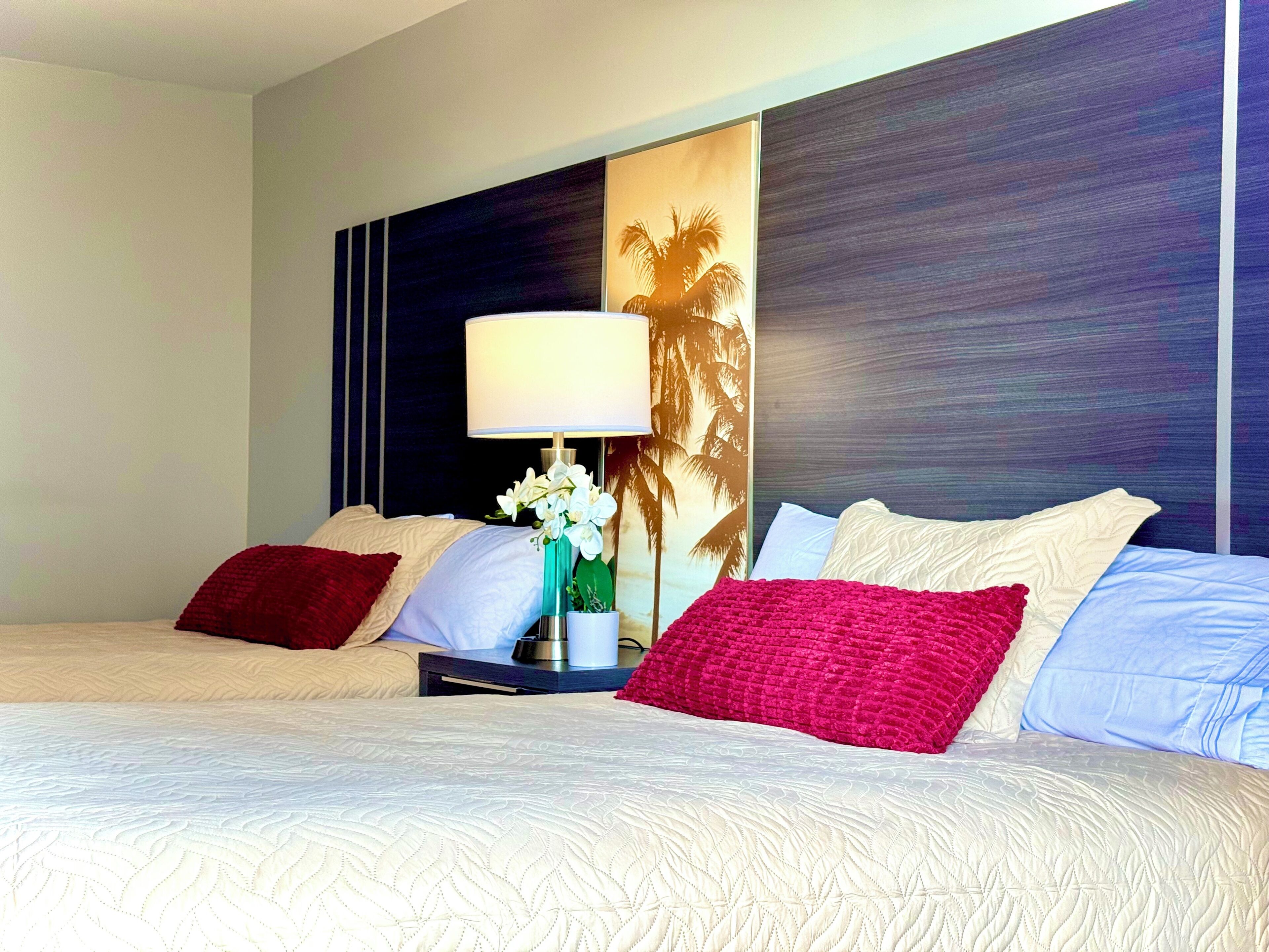 A hotel room with two beds, a nightstand with a lamp, and a large wall mural.