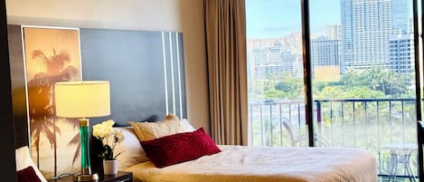 Habitación de hotel con dos camas, una mesita de noche con lámpara, un jarrón con flores y un amplio ventanal con vista a la ciudad.