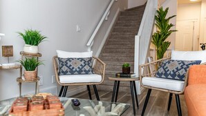 A living room with wicker chairs, a glass coffee table, and potted plants. - Luxe Escape Duo - 8 Beds - Sleeps 22 - 4 Car Garage (Edmonton)