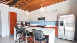A modern kitchen with a central island, bar stools, stainless steel appliances, and a wooden ceiling. - Your Perfect Tropical Vacation Villa (Guatemala de Santa Rosa)