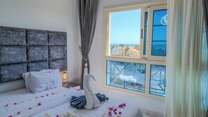 Una cama bien hecha con sábanas blancas y pétalos de flores rosa, una toalla con forma de cisne y un cabecero.