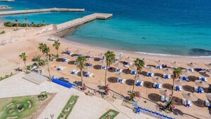 Un resort de playa con filas de tumbonas, palmeras y una vista despejada del mar.