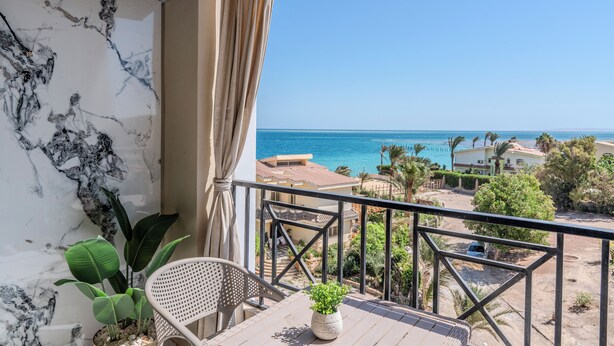 Un balcón con vista al mar, una pared de mármol y una planta en maceta.