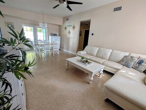 A living room with a white sofa, a coffee table, and a dining area with chairs and a table. - Dancing Seahorse Beach House with Heated Pool! (Largo)