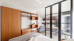 A modern hotel room with a bed, a wooden wardrobe, a grey sofa, and a balcony with a view. - Morse Residencial Flipchave MOR000 (Joinville)