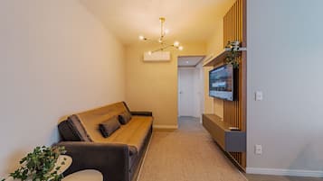 Una sala de estar moderna con un sofá, un televisor de pantalla plana montado en un panel de madera y una lámpara en el techo.