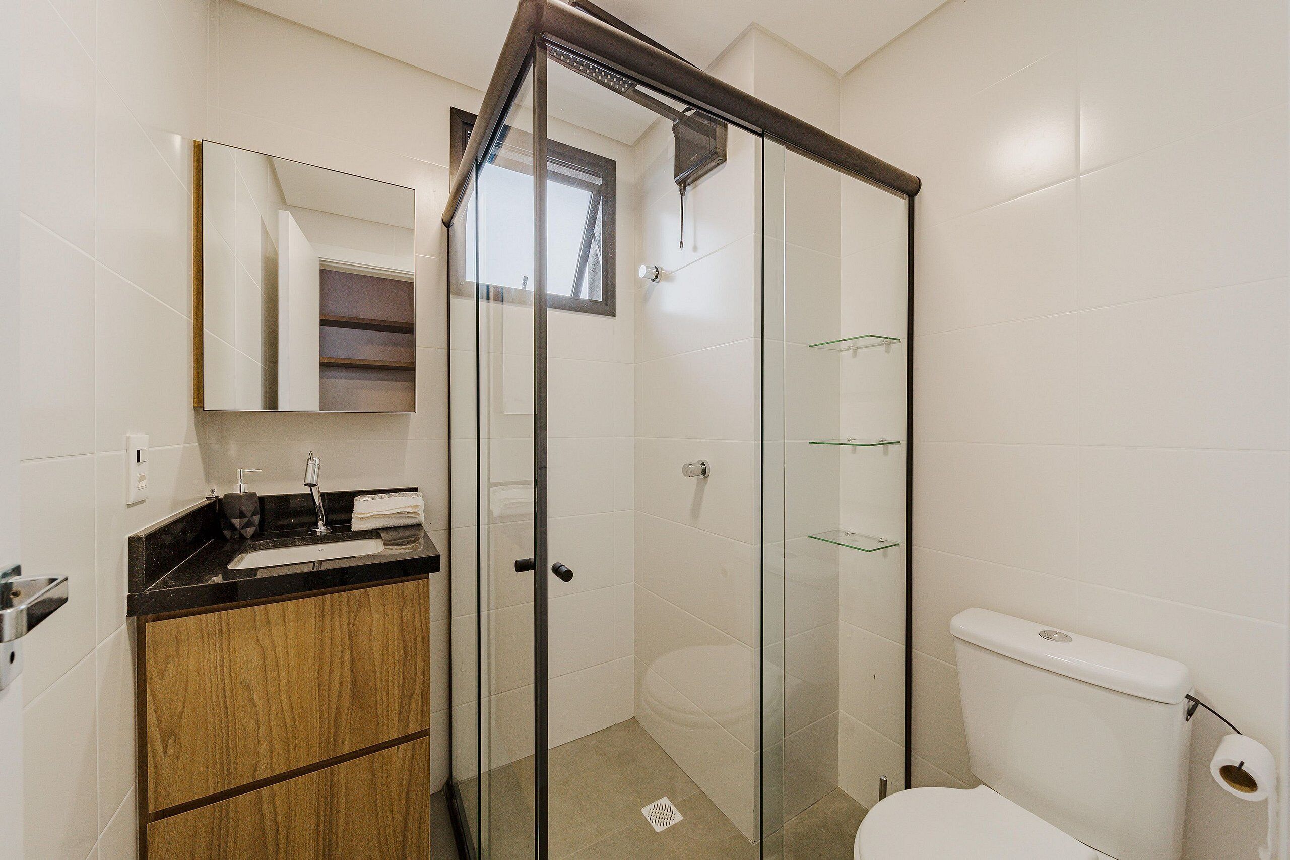 A bathroom with a glass-enclosed shower, a toilet, and a sink with a mirror above it.