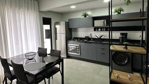 A modern kitchen with a dining area, featuring a built-in oven, microwave, and a black shelving unit with plants. - Morse Residencial Flipchave MOR000 (Joinville)