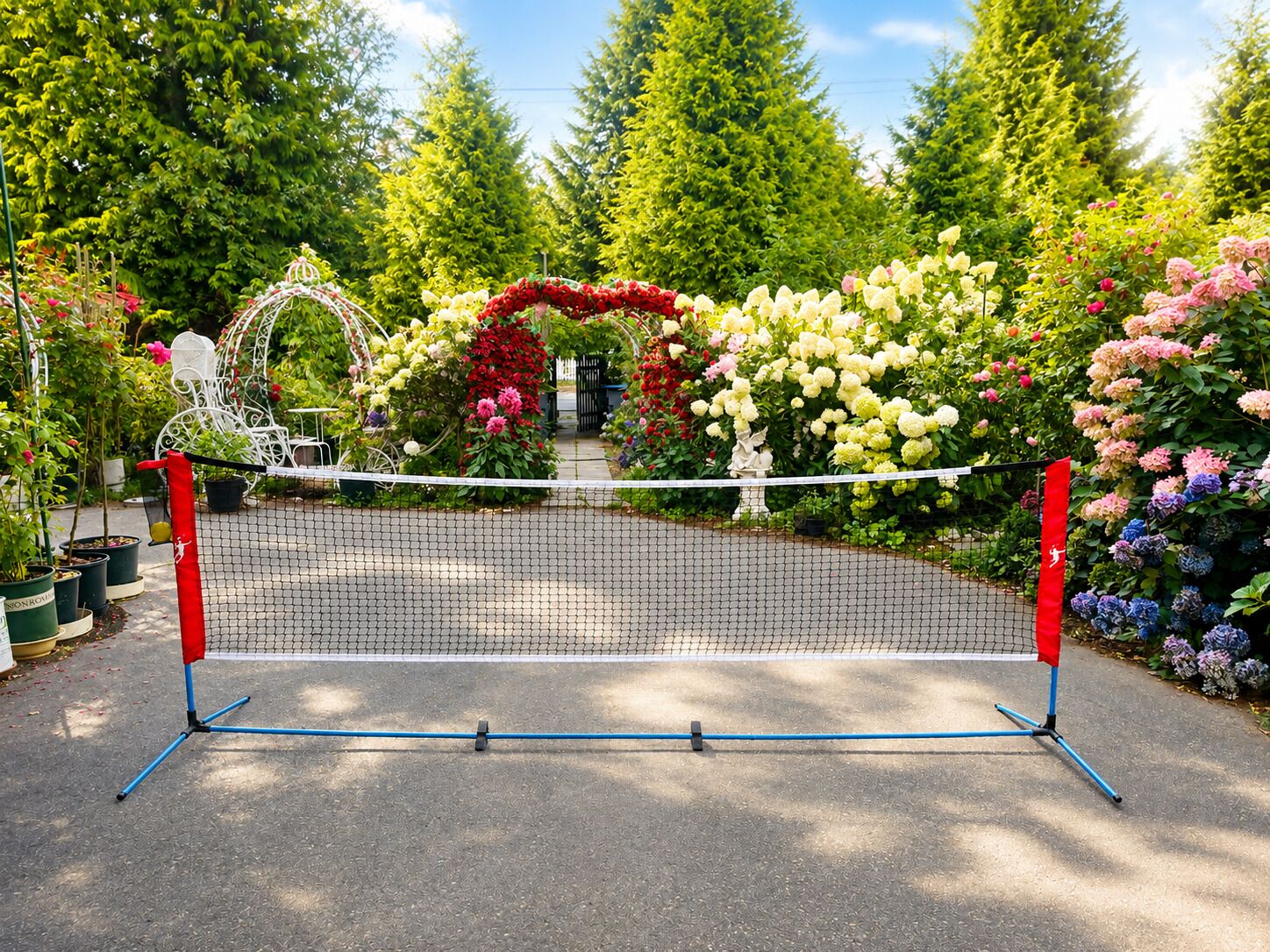 Cancha de tenis con red, rodeada de diversas plantas y árboles florecientes.