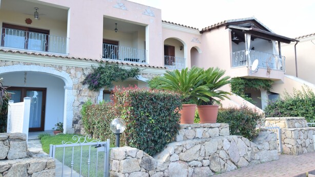 Un edificio de varios pisos con balcones, muros de piedra y plantas en macetas.