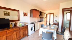 Una cocina compacta con lavadora, una mesa de comedor con sillas y un televisor sobre un mueble de madera.