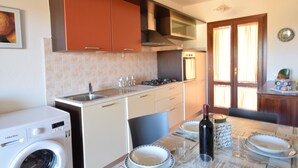 Una cocina funcional con lavadora, una mesa de comedor dispuesta con platos y una botella de vino.