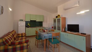 Ett kompakt bostadsutrymme med ett litet kök, en matplats med bord och stolar, en soffa och en tv som står på ett skåp.