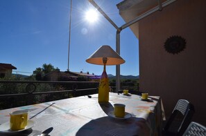 A table with a yellow lamp, two yellow cups, and a spoon on a tablecloth with a mountain view in the background. - Fagr-gai02-2p in Agrustos (Budoni)