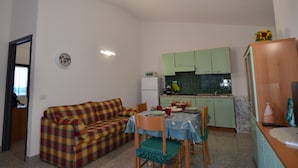 Ett kompakt bostadsutrymme med en soffa, ett matbord, stolar, ett litet kök och ett litet kylskåp.