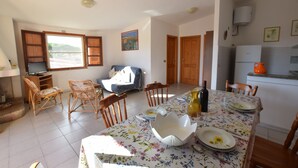 A dining area with a table set for two, wooden chairs, a sofa, and a television in the background. - Fsg-pint02p1 in San Giovanni (Posada)