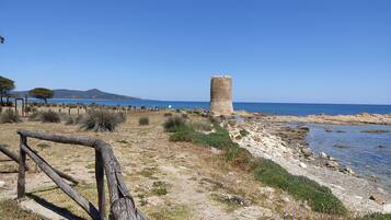 Un paisaje costero con una torre de piedra, playa arenosa y cielo azul despejado.