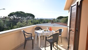 A balcony with a table and chairs, a view of trees and distant hills, and a closed door. - Fsg-pint02p1 in San Giovanni (Posada)
