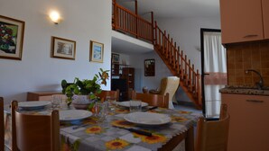 Zona pranzo con tavolo apparecchiato per quattro persone, una scala e angolo cottura.