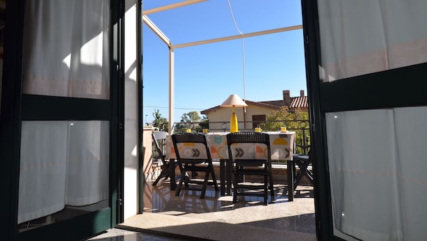 Un patio aperto con tavolo e sedie, un ombrellone giallo e vista su un edificio sullo sfondo.