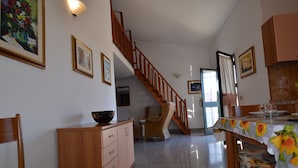 Zona pranzo con scala in legno, tavolo da pranzo con tovaglia a fiori e un mobile contenitore con cassetti.