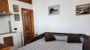 Ein Schlafzimmer mit einem Bett, einer Holztür, einem Regal mit Büchern und gerahmten Bildern an der Wand.